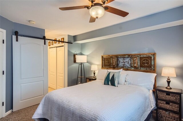 bedroom with a barn door, ceiling fan, a closet, and light carpet