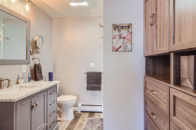 bathroom featuring hardwood / wood-style floors, vanity, toilet, and baseboard heating