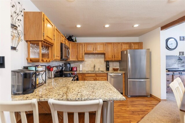 kitchen with a textured ceiling, a sink, appliances with stainless steel finishes, decorative backsplash, and light stone countertops