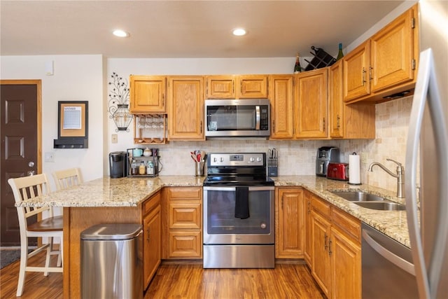 kitchen with appliances with stainless steel finishes, light stone counters, wood finished floors, a peninsula, and a sink