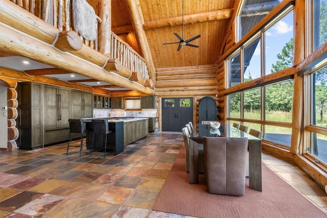 dining room with beam ceiling, rustic walls, plenty of natural light, and a towering ceiling