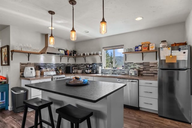 kitchen with decorative backsplash, appliances with stainless steel finishes, wall chimney exhaust hood, sink, and pendant lighting