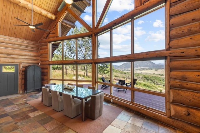 unfurnished sunroom with ceiling fan, lofted ceiling with beams, wooden ceiling, a mountain view, and plenty of natural light