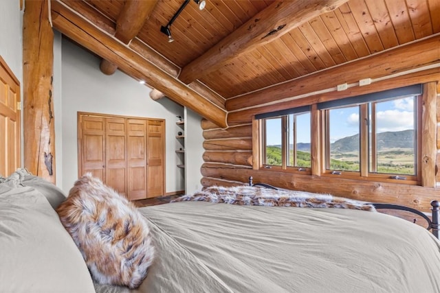 bedroom with log walls, beamed ceiling, a mountain view, track lighting, and wood ceiling