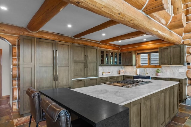 kitchen with a center island, sink, stainless steel gas cooktop, beamed ceiling, and backsplash