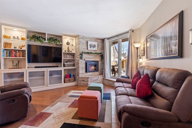 living room with built in shelves, a stone fireplace, and hardwood / wood-style flooring