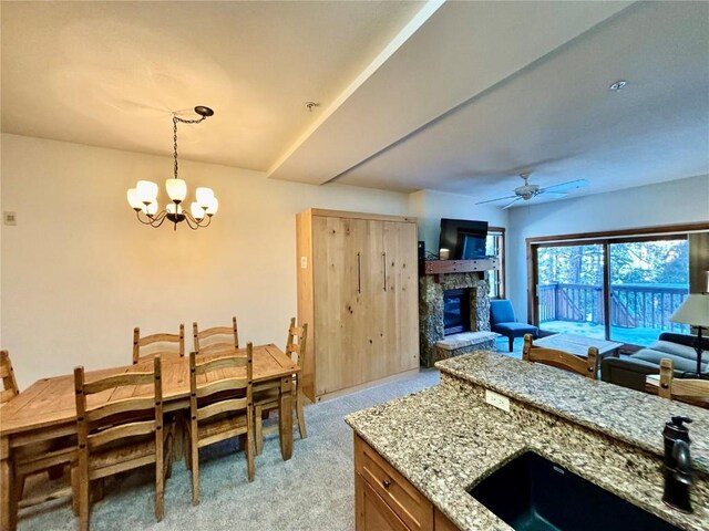 interior space with light stone counters, ceiling fan with notable chandelier, light colored carpet, a stone fireplace, and hanging light fixtures