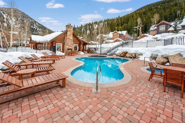 snow covered pool featuring a patio area, fence, a mountain view, and a fenced in pool