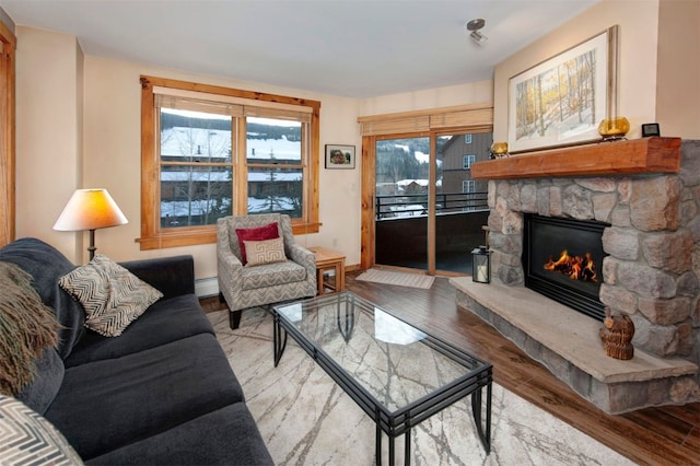 living room with a baseboard radiator, a stone fireplace, and light wood-type flooring