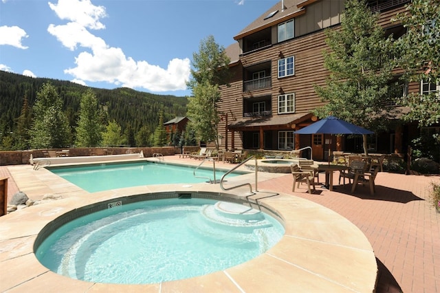 view of swimming pool with a community hot tub, a mountain view, and a patio area