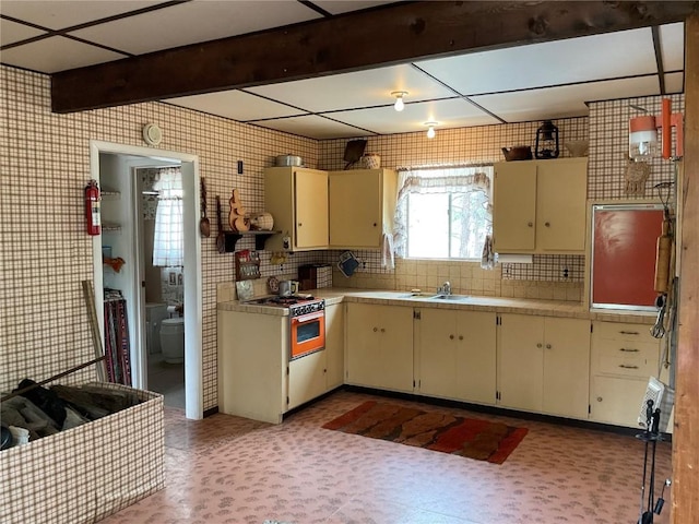 kitchen with white gas stove, tasteful backsplash, and cream cabinets