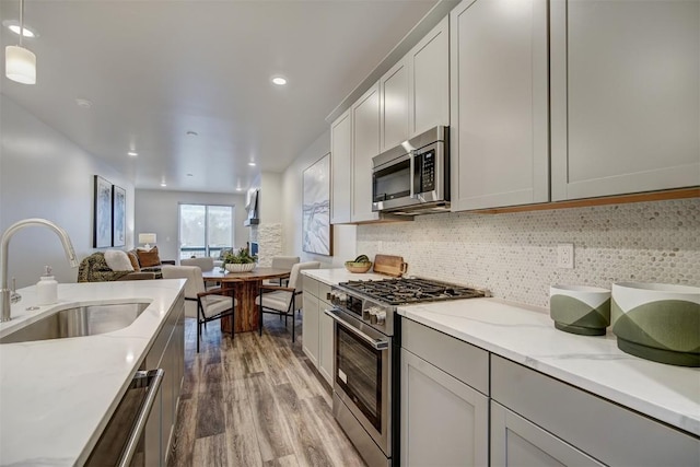 kitchen with backsplash, light stone counters, stainless steel appliances, sink, and decorative light fixtures