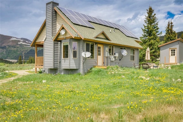 view of front facade with a mountain view, roof mounted solar panels, an outbuilding, and a chimney