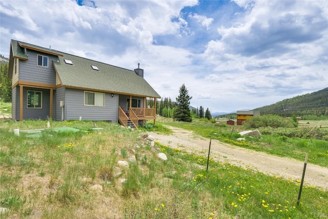 back of property with a chimney, driveway, and a shingled roof