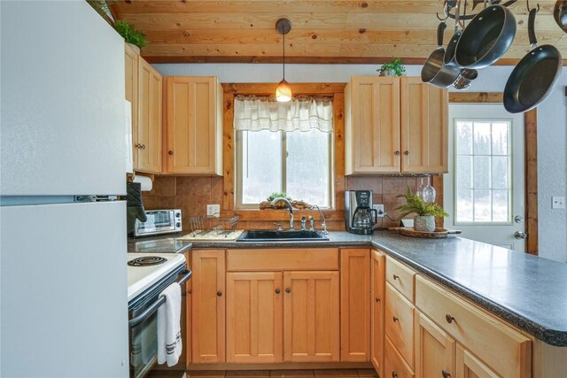 kitchen with a peninsula, freestanding refrigerator, a sink, electric stove, and dark countertops