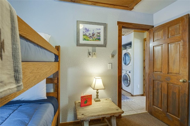 carpeted bedroom featuring tile patterned flooring, stacked washing maching and dryer, and a textured wall