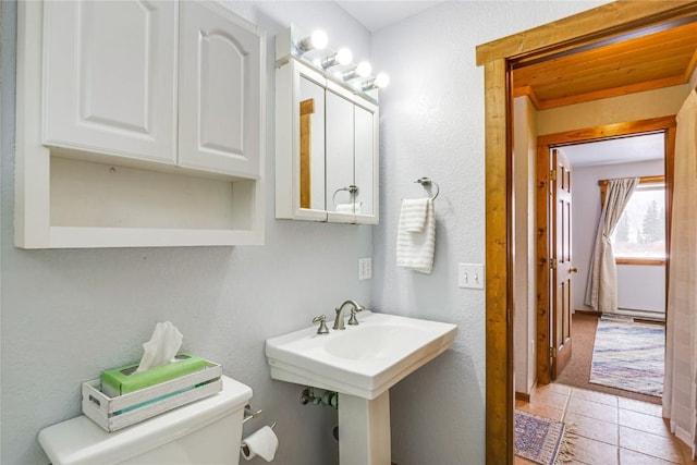 bathroom featuring tile patterned flooring, toilet, a textured wall, and a sink