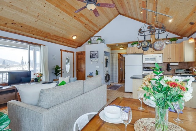 living area with a ceiling fan, high vaulted ceiling, light tile patterned flooring, wood ceiling, and stacked washer and clothes dryer