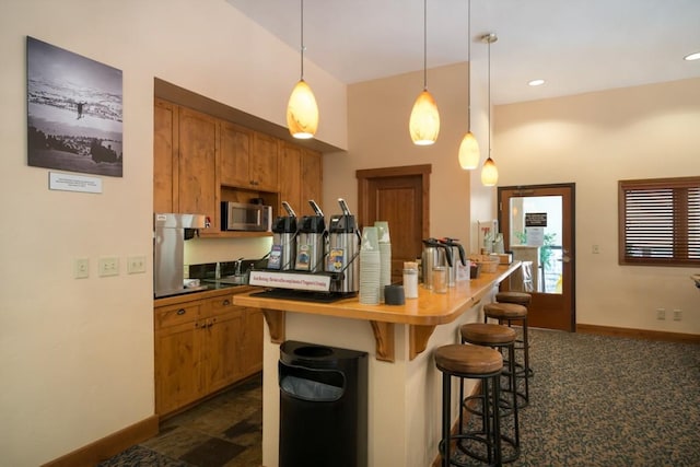 kitchen with dark colored carpet, hanging light fixtures, and a breakfast bar area