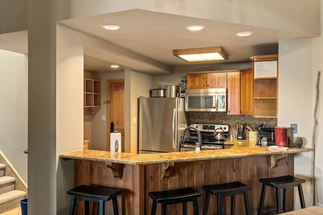 kitchen featuring stainless steel appliances, tasteful backsplash, a kitchen breakfast bar, light stone counters, and kitchen peninsula