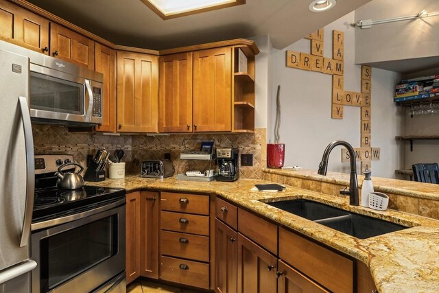 kitchen with backsplash, light stone counters, sink, and stainless steel appliances