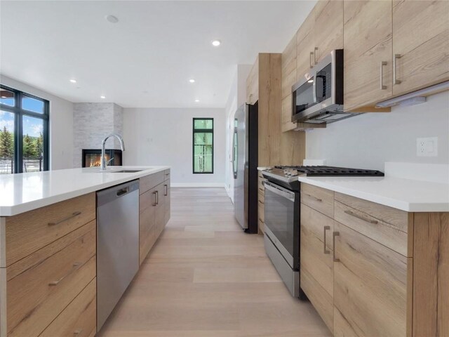 kitchen with sink, a kitchen island with sink, stainless steel appliances, light hardwood / wood-style floors, and light brown cabinetry