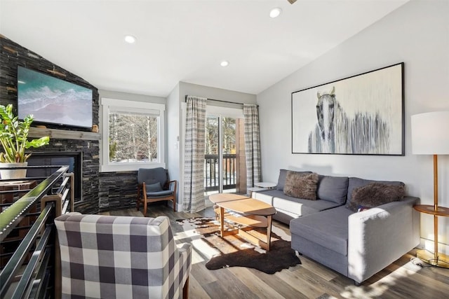 living area featuring lofted ceiling, recessed lighting, wood finished floors, and a stone fireplace