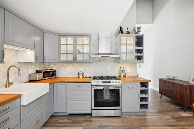 kitchen with stainless steel appliances, glass insert cabinets, wooden counters, and wall chimney range hood