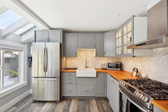 kitchen with stainless steel appliances, wooden counters, wall chimney range hood, and a sink