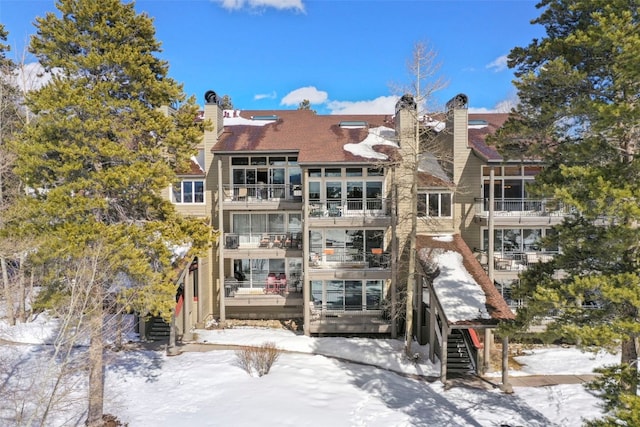 snow covered back of property with a chimney and stairs