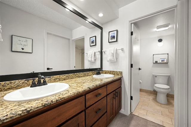 bathroom featuring double vanity, a sink, toilet, and baseboards