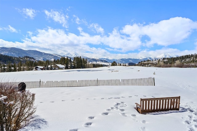 yard layered in snow with a mountain view and fence