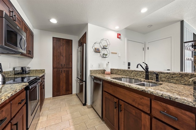 kitchen with stone countertops, stainless steel appliances, a textured ceiling, a sink, and recessed lighting