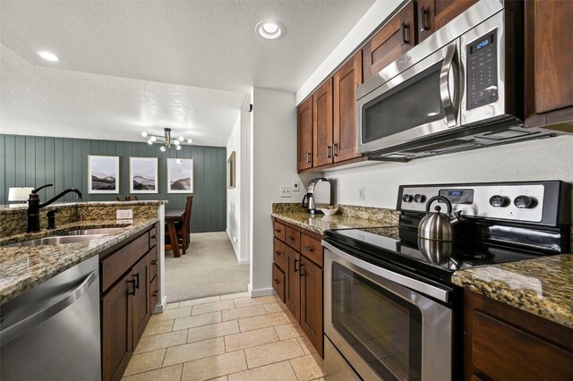 kitchen with dark stone countertops, an inviting chandelier, stainless steel appliances, a textured ceiling, and a sink