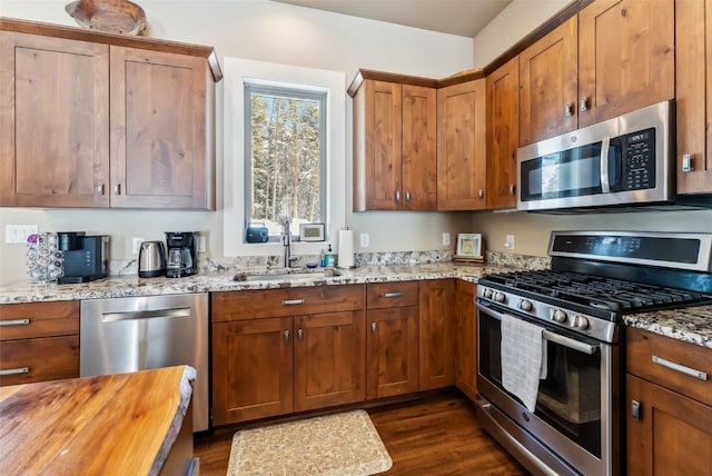 kitchen with wood counters, appliances with stainless steel finishes, brown cabinets, dark wood-type flooring, and a sink