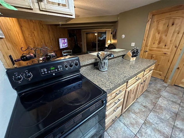 kitchen with light tile patterned floors, wood walls, black electric range, a textured ceiling, and light brown cabinets