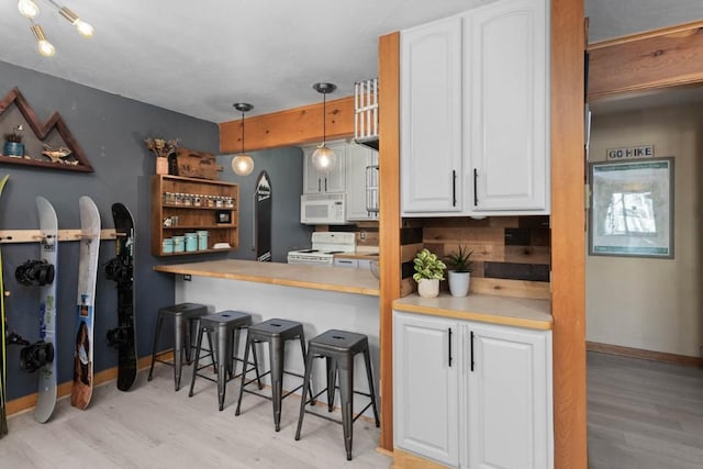 kitchen featuring white appliances, white cabinets, hanging light fixtures, kitchen peninsula, and a breakfast bar area