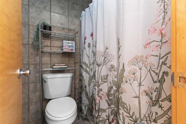 bathroom featuring a shower with shower curtain, toilet, and tile walls