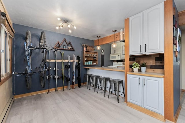 kitchen with kitchen peninsula, a kitchen breakfast bar, white appliances, a baseboard heating unit, and decorative light fixtures