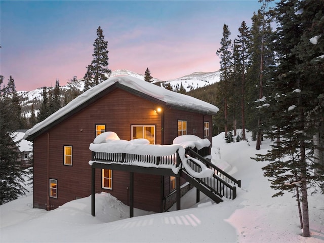 snow covered back of property featuring stairs and a wooden deck