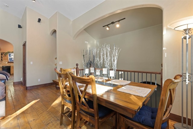 dining space with lofted ceiling, hardwood / wood-style flooring, baseboards, and arched walkways