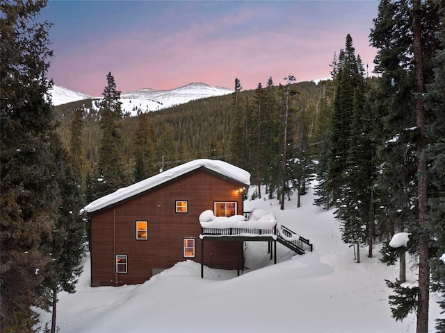 view of snow covered exterior featuring a deck with mountain view, a view of trees, and stairs