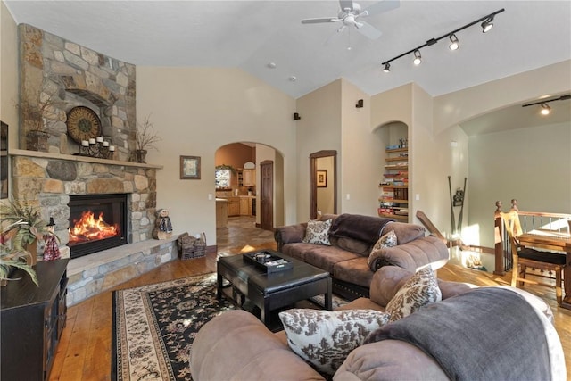 living room featuring lofted ceiling, a stone fireplace, light wood-type flooring, track lighting, and ceiling fan