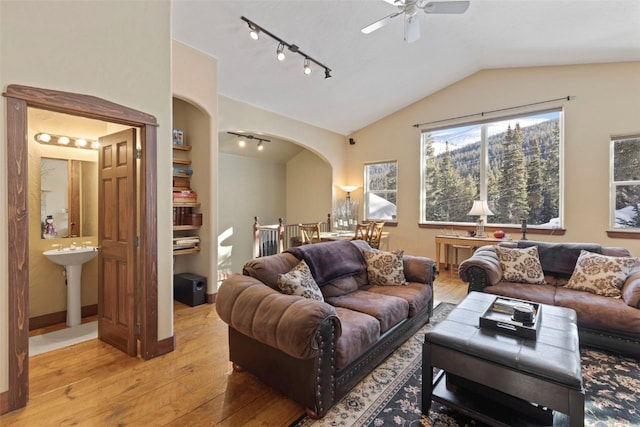 living area with arched walkways, lofted ceiling, light wood-style flooring, ceiling fan, and track lighting