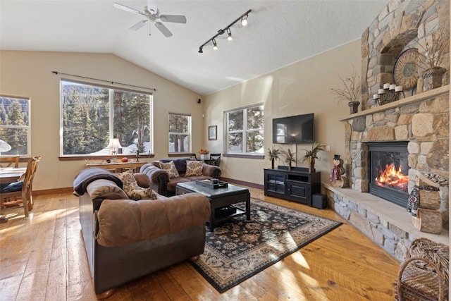 living room with hardwood / wood-style floors, a stone fireplace, vaulted ceiling, and ceiling fan