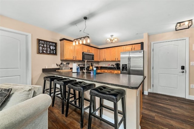 kitchen featuring kitchen peninsula, dark hardwood / wood-style flooring, a breakfast bar, stainless steel appliances, and decorative light fixtures