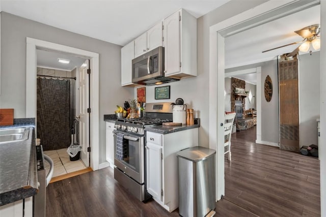 kitchen featuring dark wood-style floors, stainless steel appliances, dark countertops, a ceiling fan, and white cabinetry