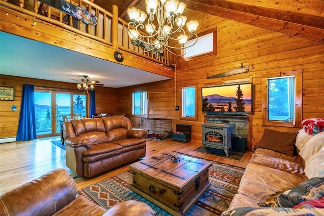 living room with lofted ceiling, wood-type flooring, a wood stove, and ceiling fan with notable chandelier