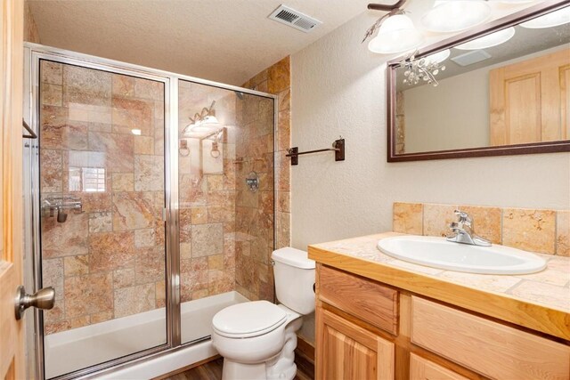 bathroom with vanity, toilet, a shower with shower door, and a textured ceiling