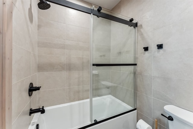 full bath with toilet, tile walls, and shower / bath combination with glass door